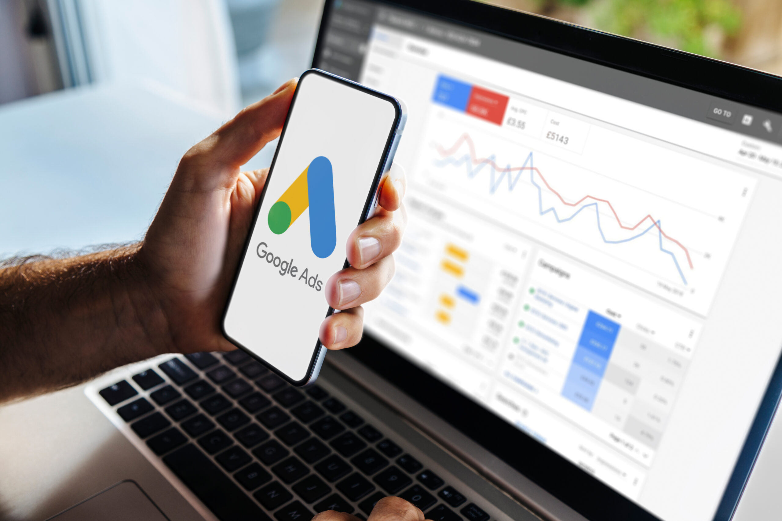 Man using a mobile phone with Google Ads on the screen and in the background a computer showing ad statistics. Rosario, Argentina – February 28, 2024. Google search ADs for business